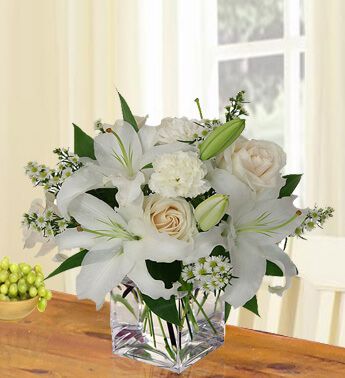 One sided round arrangement of 2 White Lilies , 4 Peach Roses , 4 White Carnations in a cube vase Soft Blooms