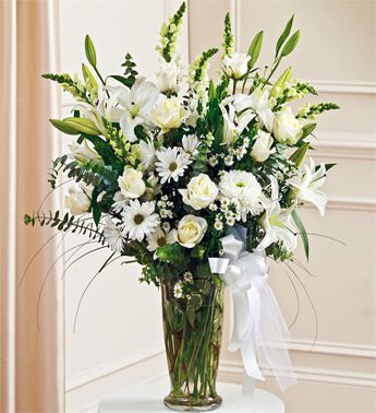 7 stems of White Lilies, 4 stems of White Chrysanthemums, 10 White Rose, 5 White Carnation in vase with greens. Perfect Tribute