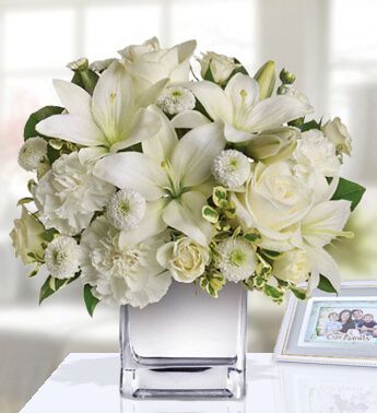 Vase with 2 stems of White Lilies , 4 White Roses , 4 White Carnations and 3 stems of Chrysanthemum (one sided round arrangement) Classically Stunner